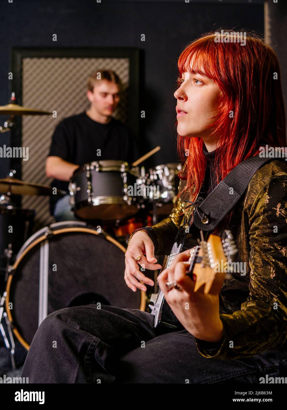 Giovane donna rossa che suona chitarra elettrica e un batterista maschile in uno studio di registrazione. Foto Stock