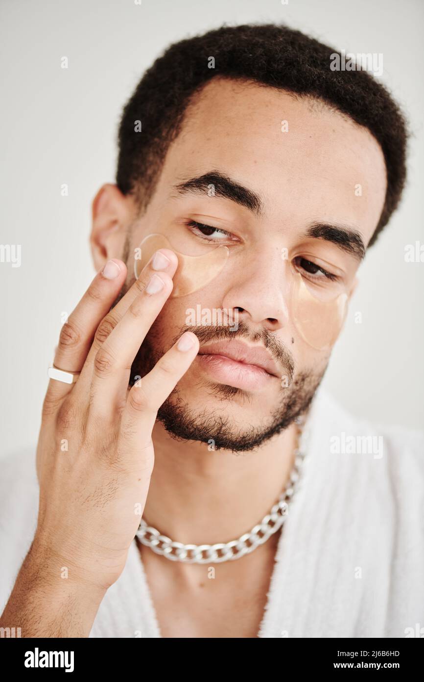 Ritratto di giovane bell'uomo che eleva la sua pelle sotto gli occhi con le macchie degli occhi Foto Stock