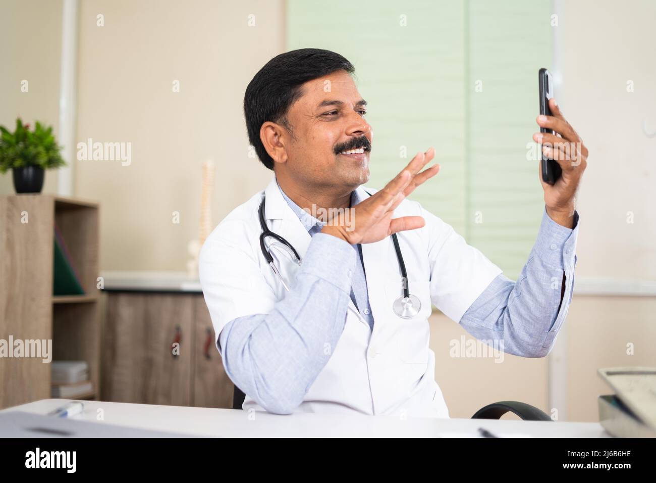 Medico in videochiamata con il paziente sul telefono cellulare in ospedale - concetto di salute, consulenza medica visruale e tecnologia Foto Stock