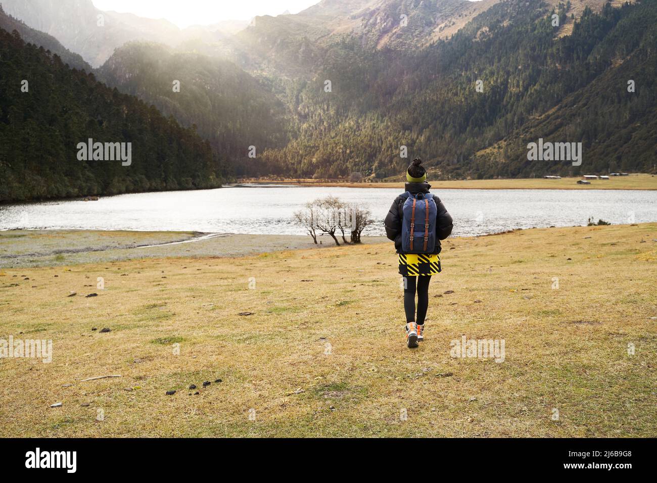 vista posteriore di donna asiatica turista a piedi verso un lago ai piedi di una montagna Foto Stock