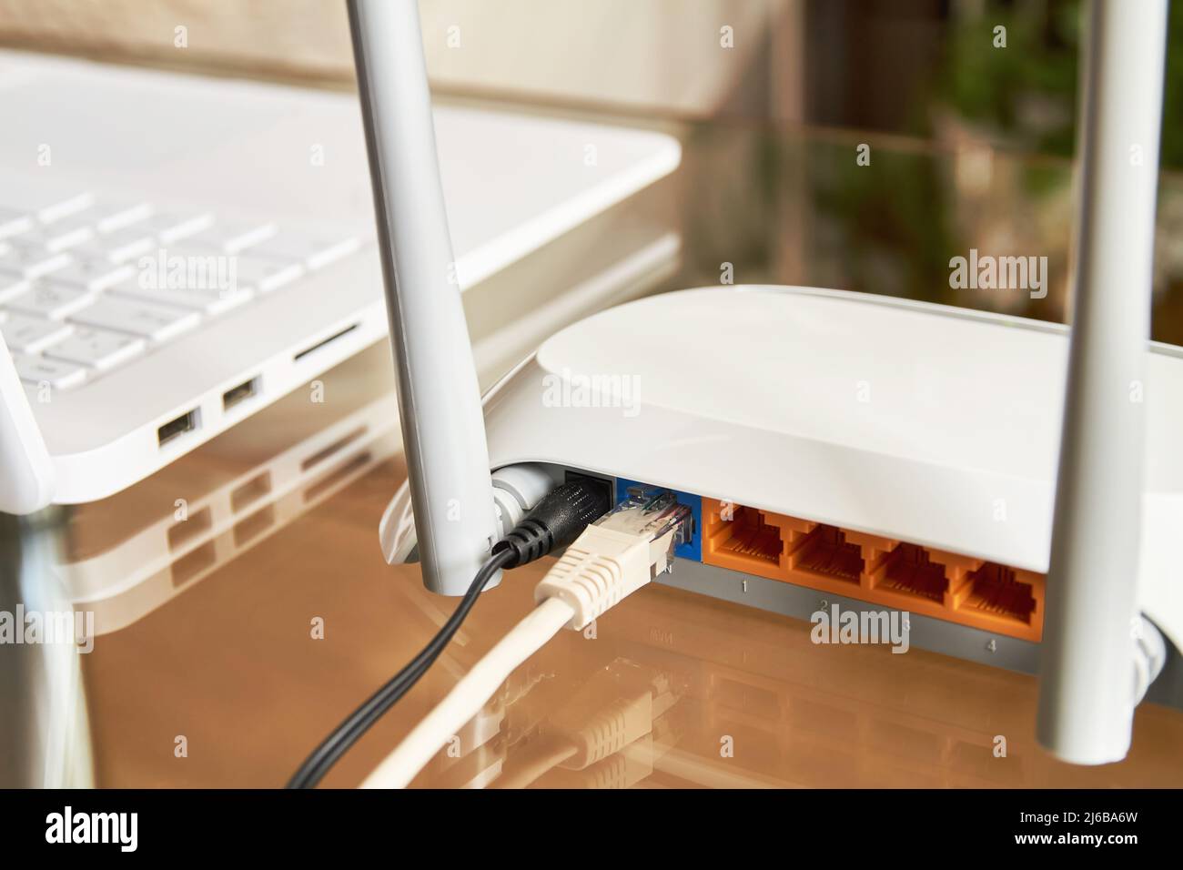 Router wi-fi wireless bianco vicino a un computer portatile su un vetro tabella Foto Stock