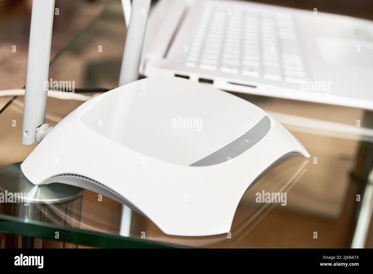 Router wi-fi wireless bianco vicino a un computer portatile su un vetro tabella Foto Stock