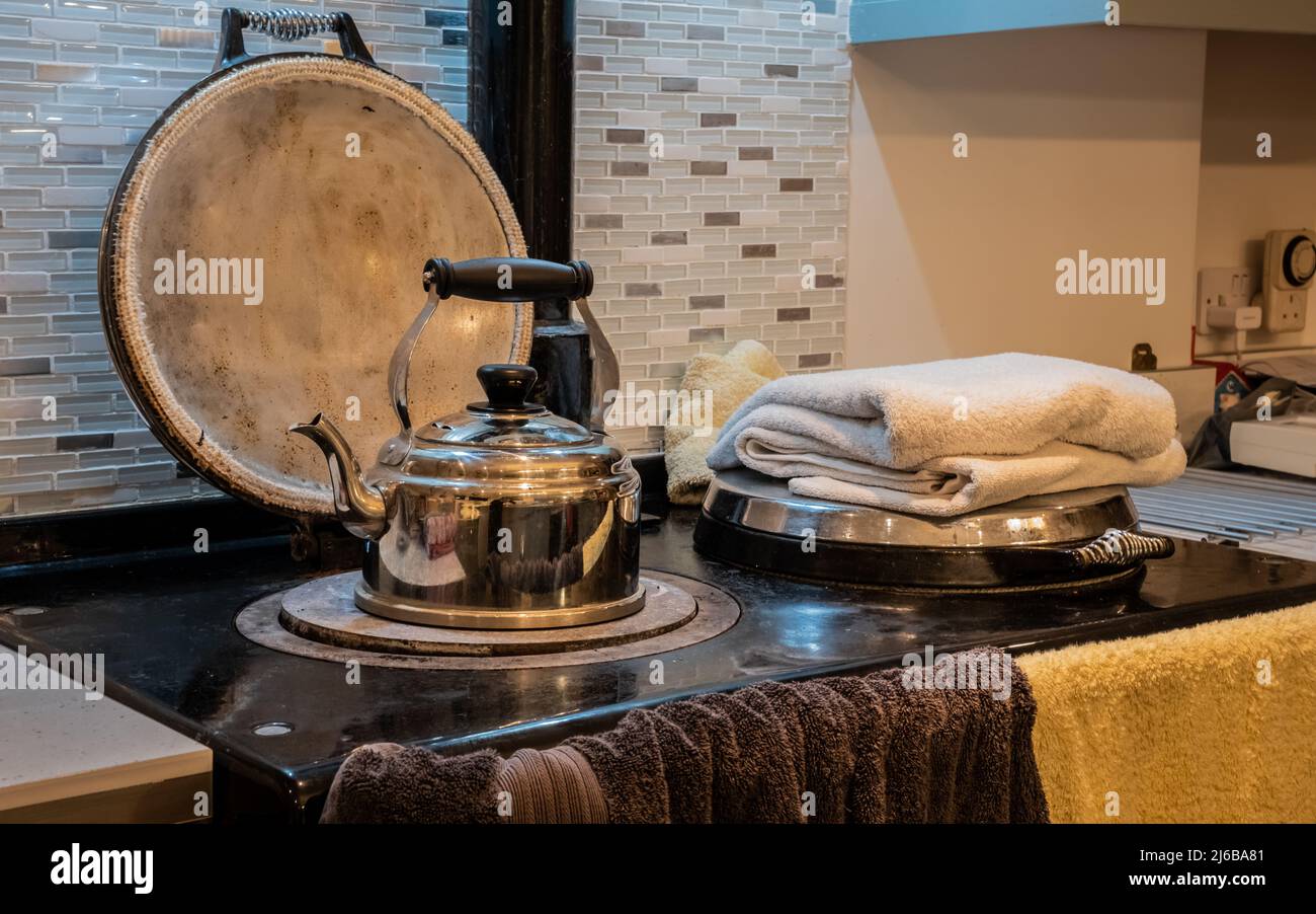 Un bollitore in metallo che riscalda e asciuga gli asciugamani su una vecchia stufa da cucina la sera Foto Stock