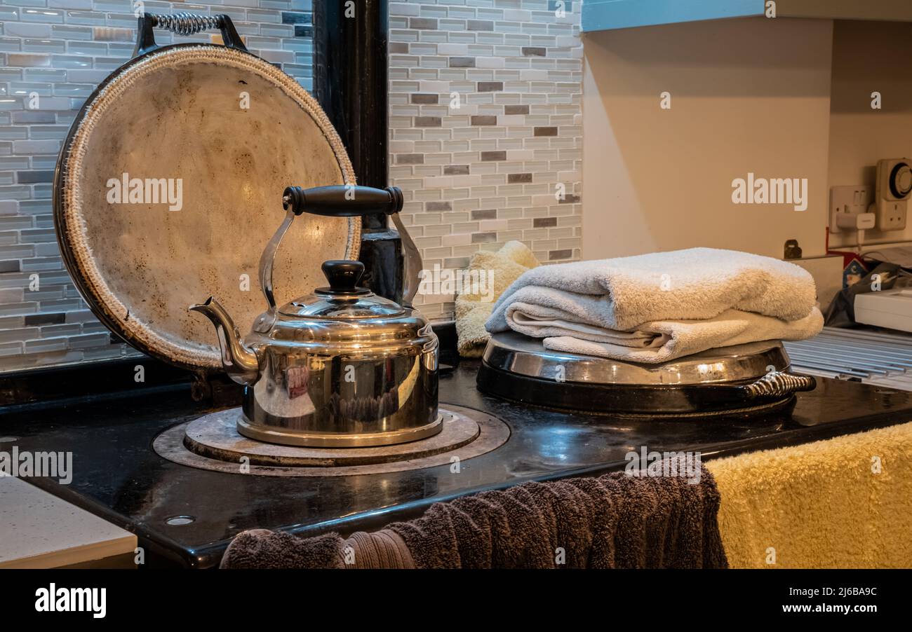 Un bollitore in metallo che riscalda e asciuga gli asciugamani su una vecchia stufa da cucina la sera Foto Stock