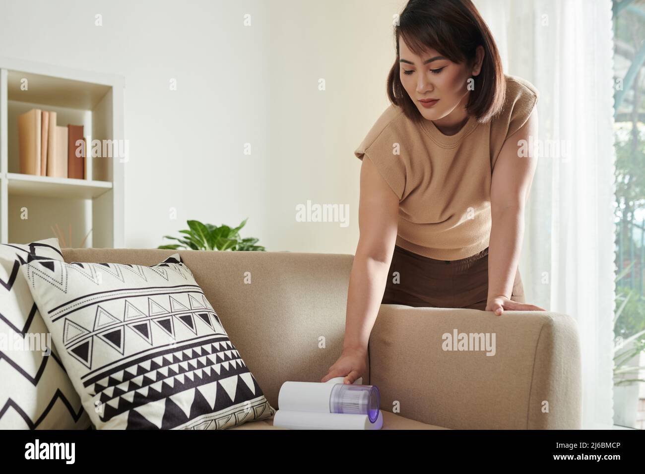 Donna asiatica che aspira il divano con pulitore per tappezzeria per  sbarazzarsi di polvere e macchie Foto stock - Alamy