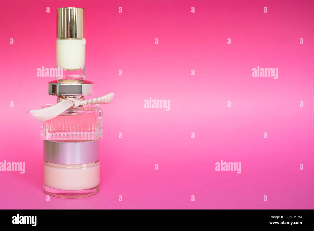 Bottiglia di profumo in vetro rosa, crema facciale e prodotto per la cura delle unghie su sfondo rosa. Bottiglia di profumo femminile, cura della pelle, cosmetica, spazio libero per il testo. Foto Stock