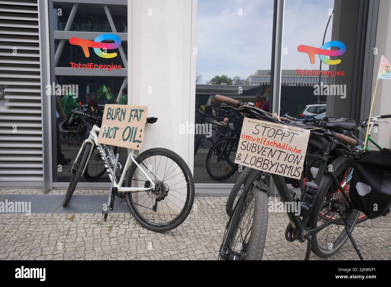 30 aprile 2022, Berlino: Striscioni di attivisti per la pace e l'ambiente con l'iscrizione "Burn Fat Not Oil" e "TOP Environmentally Nocal Grant & lobbying" sono visti di fronte alla sede della compagnia petrolifera francese Total. Per quanto riguarda le biciclette, le biciclette da carico e i tandem, chiedono una politica dei trasporti a Berlino e in altre dieci grandi città tedesche che risparmiino petrolio al fine di ridurre la dipendenza dalla Russia e allentare un embargo sul petrolio. Foto: Joerg Carstensen/dpa Foto Stock
