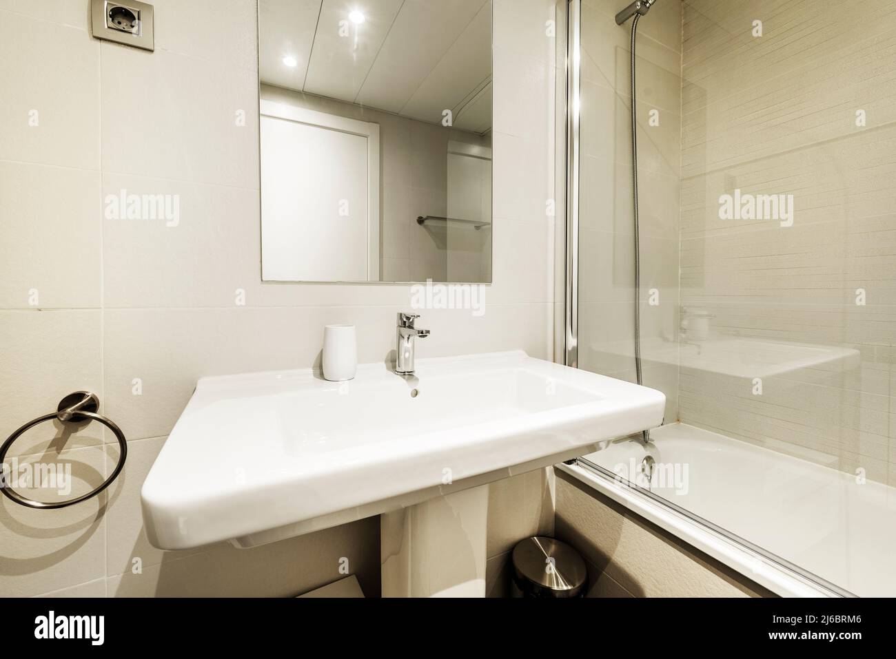 Bagno con lavandino in porcellana bianca su piedistallo in porcellana, specchio senza cornice, vasca in vetro e piastrelle chiare Foto Stock
