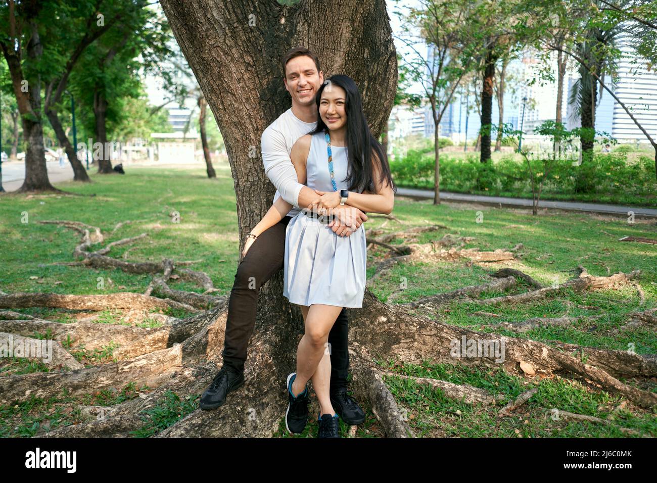 Coppia multirazziale sposata di recente che si abbraccia contro un albero Foto Stock