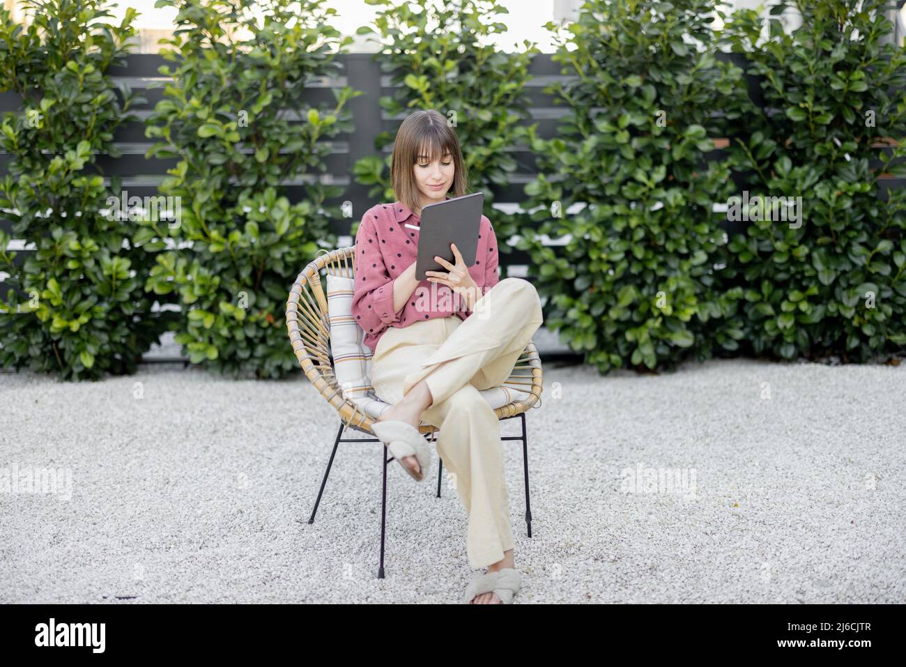 Donna che lavora su un tablet digitale mentre si siede in un cortile rilassato Foto Stock