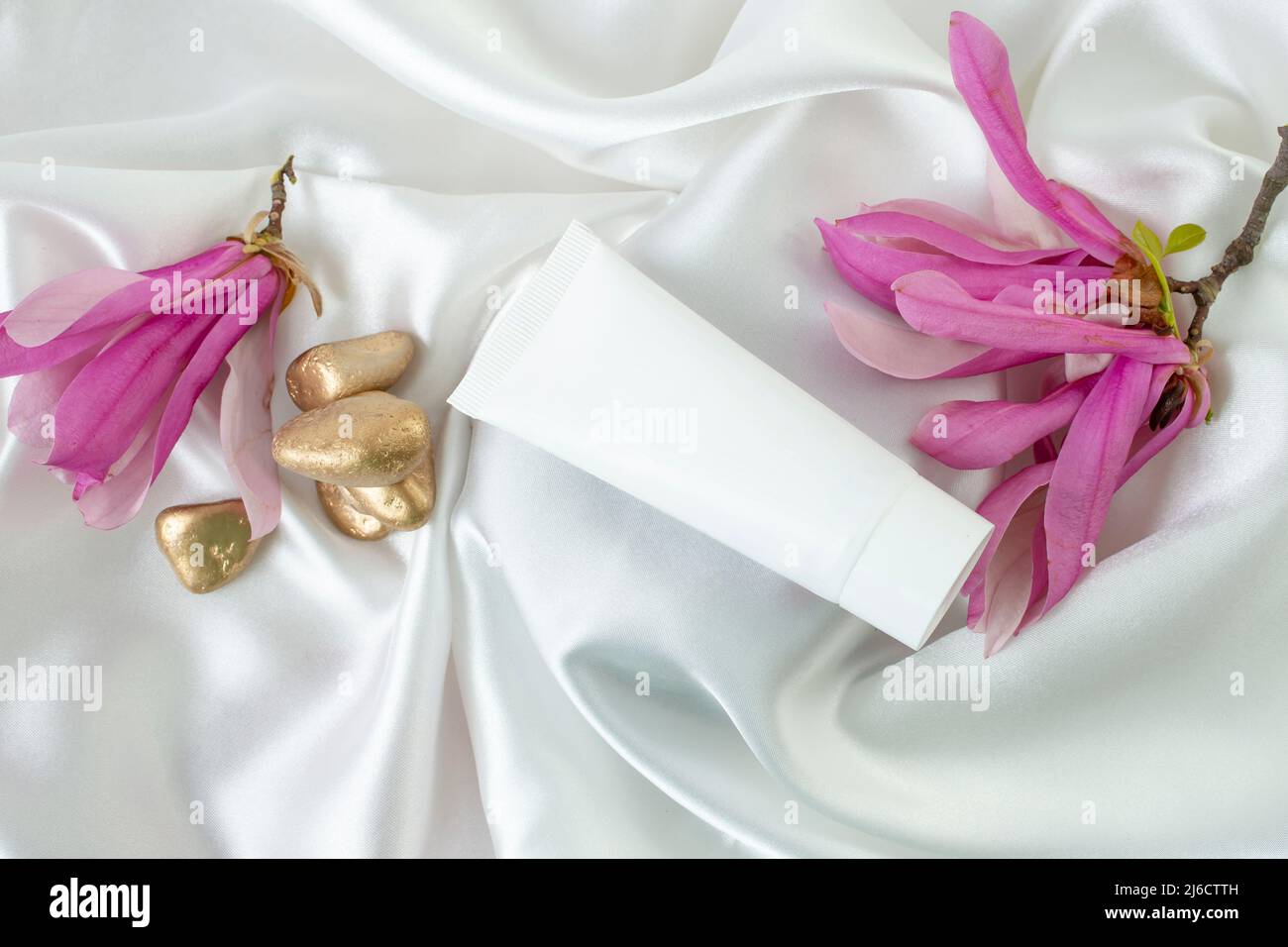 Sfondo cosmetico fotografico prodotto, con fiori magnolia su sfondo bianco satinato tessuto Foto Stock