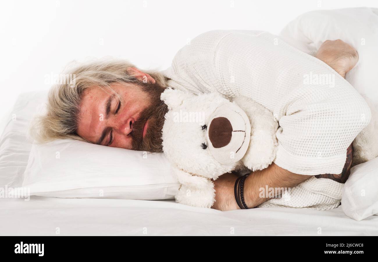 Uomo bearded che dorme in letto comodo con orsacchiotto. Sogni dolci. Fine settimana mattina. Foto Stock