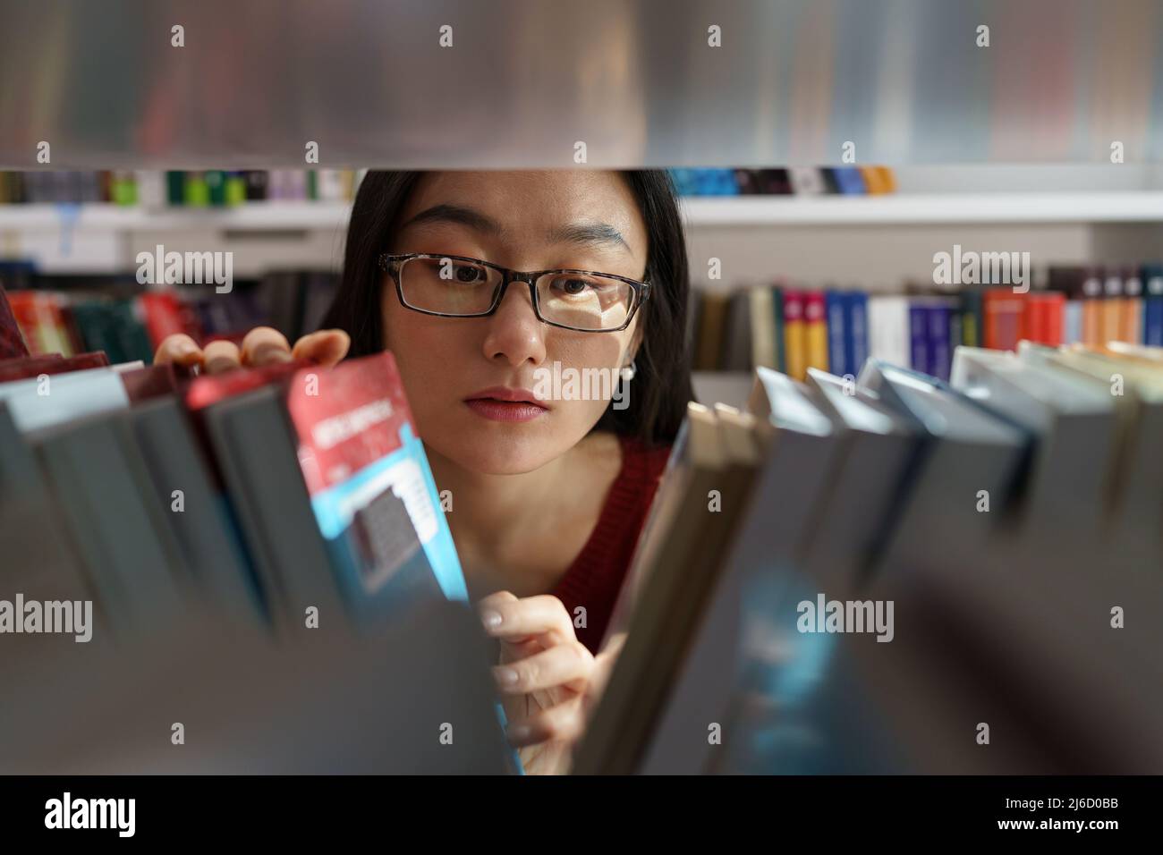 Giovane ragazza asiatica del college alla ricerca di riviste accademiche, libri e fonti primarie in biblioteca Foto Stock