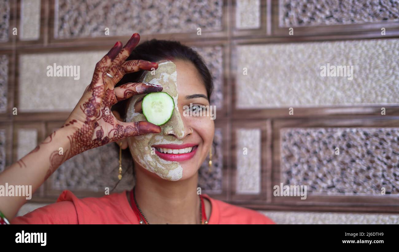 Una donna con maschera facciale e fresco cetriolo sugli occhi, rilassante a casa. Primo piano ritratto di sorridente ragazza in maschera di argilla. Mitti mitti fatti in casa miti viso pac Foto Stock