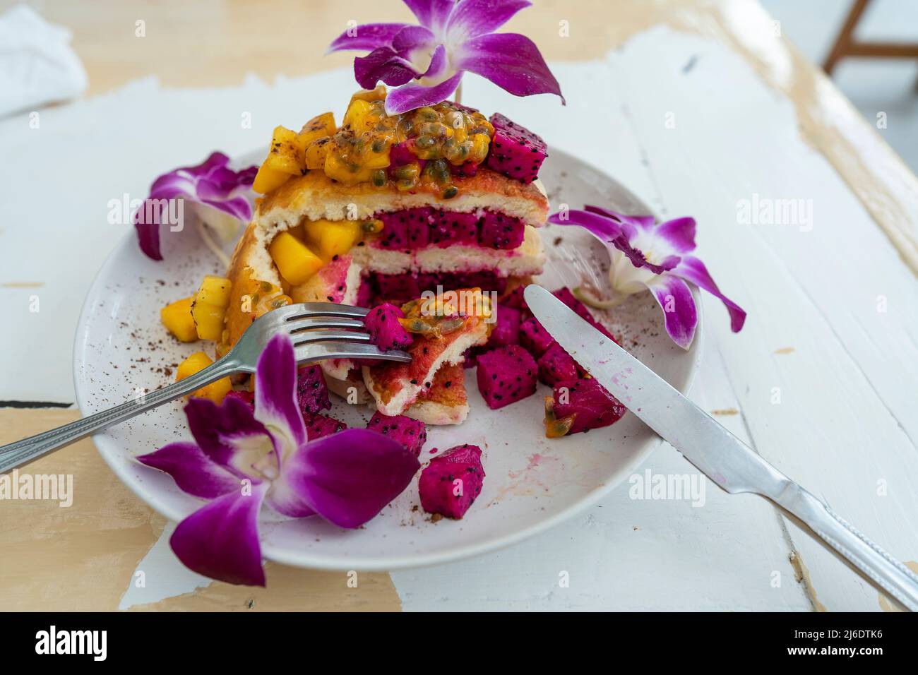 Gustosi pancake con frutta tropicale in un piatto su un tavolo in un caffè, primo piano. Colazione sana. Deliziosi pancake con mango, frutta di drago e pass Foto Stock
