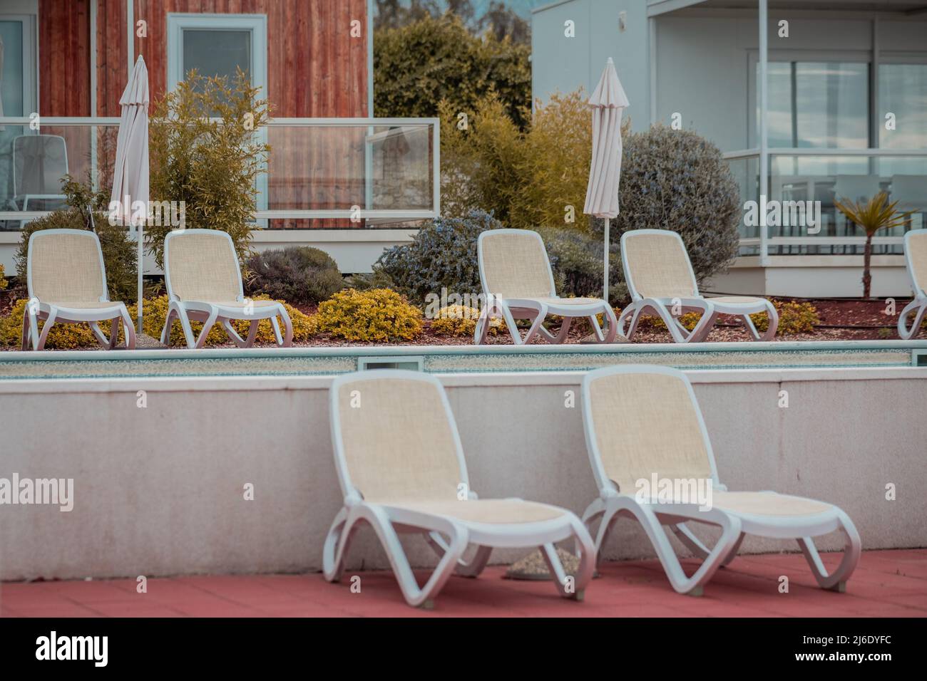 Moltitudine di sedie a sdraio vuote con nessuno seduto su di loro in un resort elegante con moderni cottage estivi sullo sfondo. Foto Stock