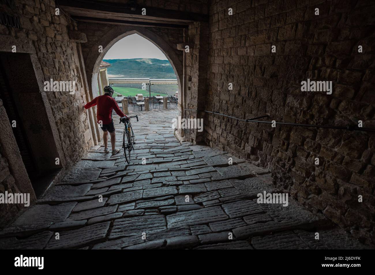 Ciclista stradale con scarpe clip in lotta per camminare sulle pietre scivolose nella città medievale istriana di Motovuin. Foto Stock