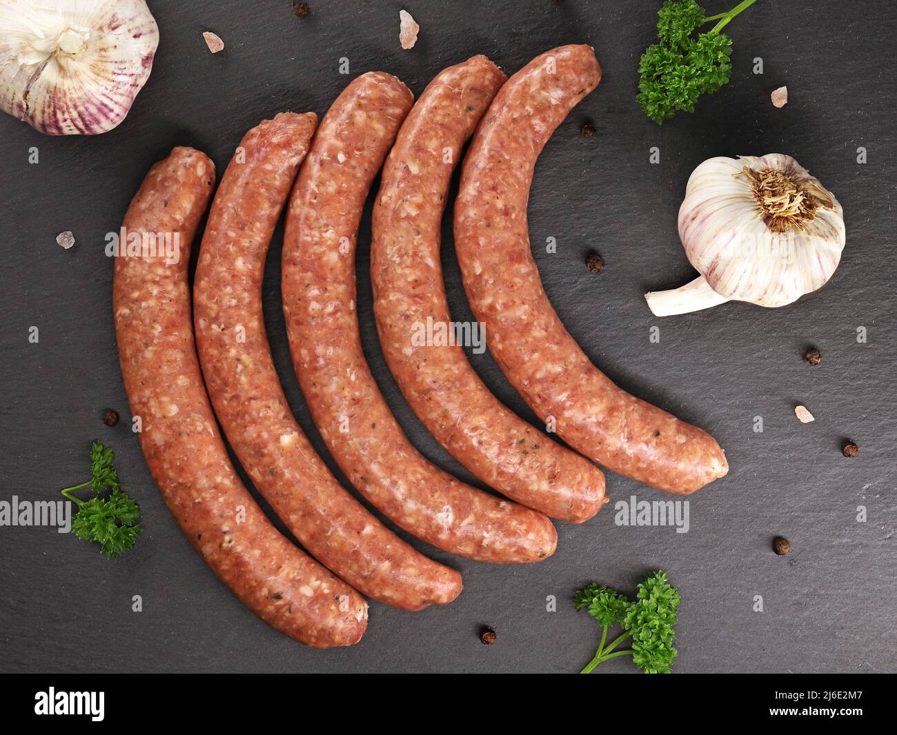 Salsicce di vitello crudo con prezzemolo, aglio e spezie in ardesia nera, vista dall'alto di deliziose salsicce rosse pronte per la cottura alla griglia Foto Stock