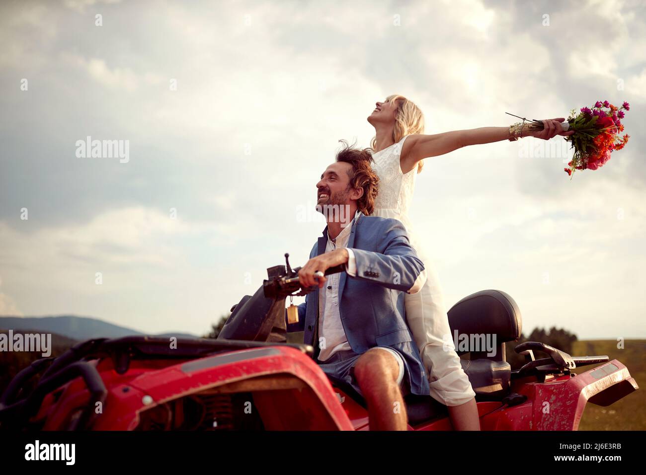 Sposi felici che guidano il quad insieme nella natura; concetto di matrimonio rurale Foto Stock