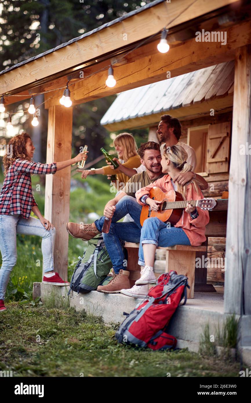 Un gruppo di amici allegri che si divertono a portico cottage nella foresta in una bella giornata. Vacanza, natura, cottage, amicizia Foto Stock