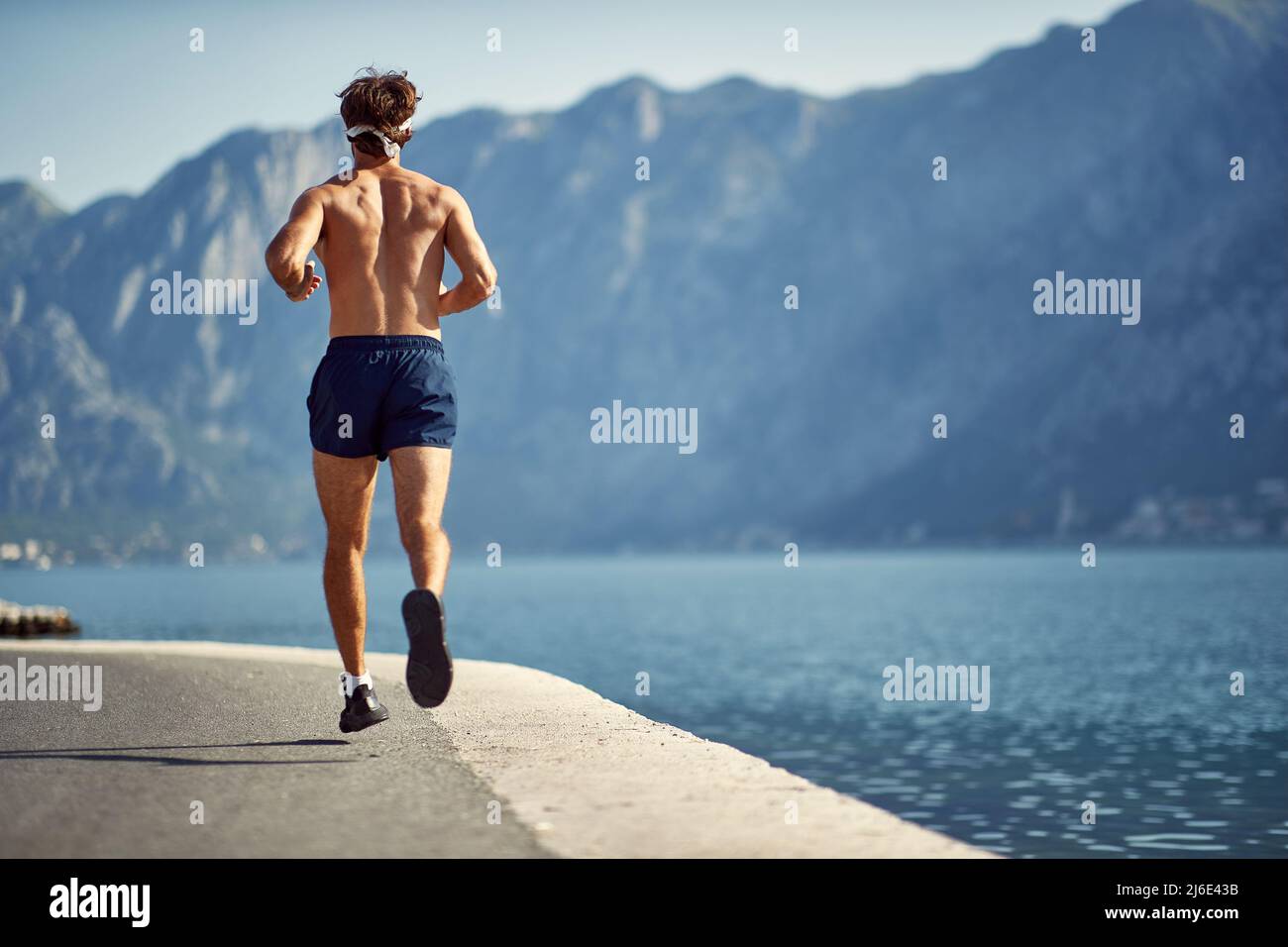 Giovane uomo che corre sul molo dall'acqua. Sport, vitalità, concetto di ricreazione. Foto Stock