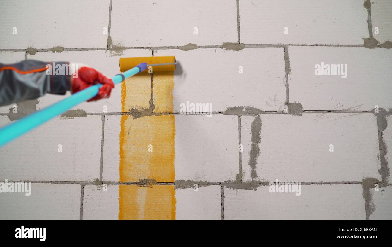 Primer parete con primer arancione. Una mano con un rullo innesca la parete levigata con una Malta durante la revisione dei locali, la fase manuale del Foto Stock