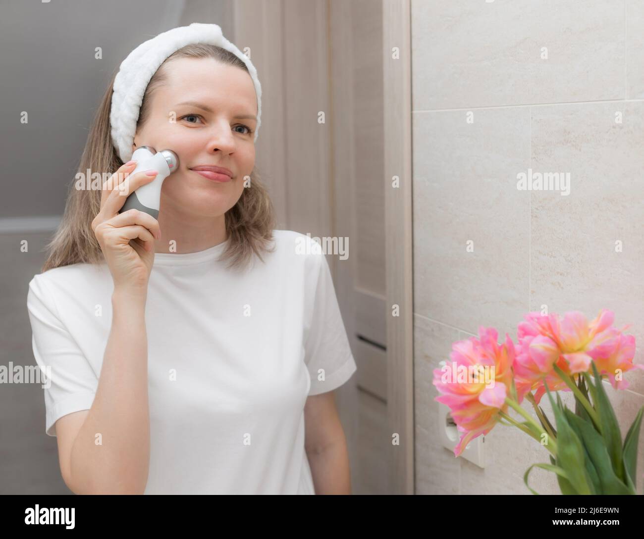 donna che si prende cura della pelle del viso con un dispositivo a microcorrente Foto Stock