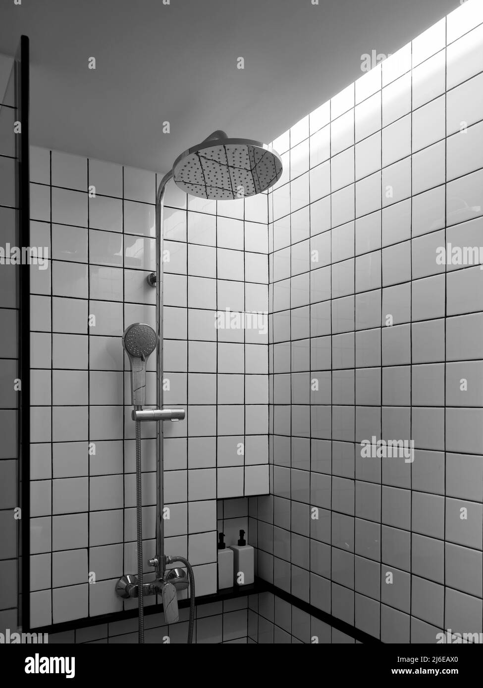 Doccia cromata con doccia a pioggia su pareti in griglia bianca e nera, l'interno della moderna box doccia nell'angolo bagno, verti Foto Stock