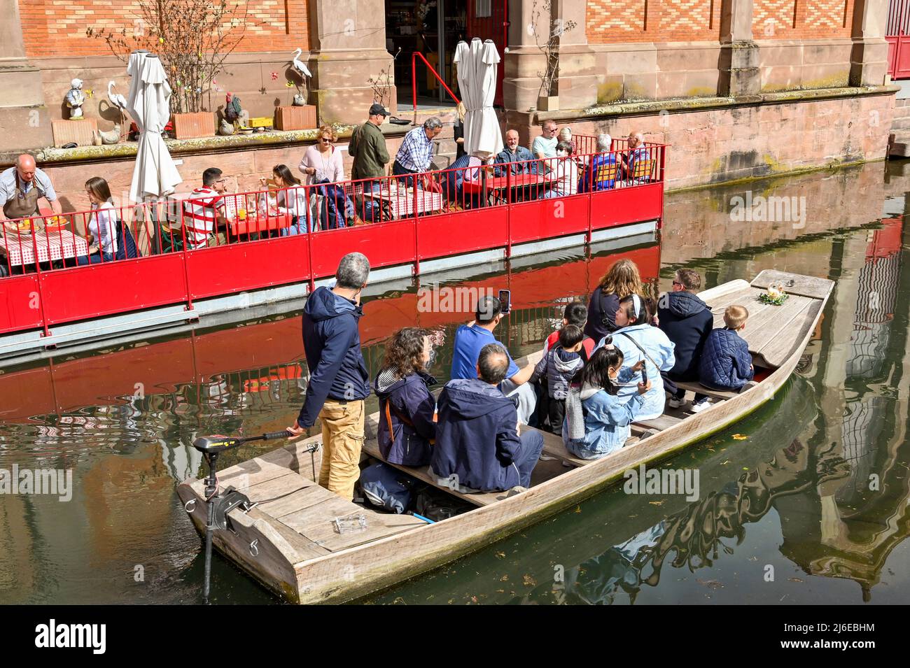 Colmar, Francia - Aprile 2022: Turisti in una piccola barca sul canale che passa le persone seduti ai tavoli di un caffè Foto Stock