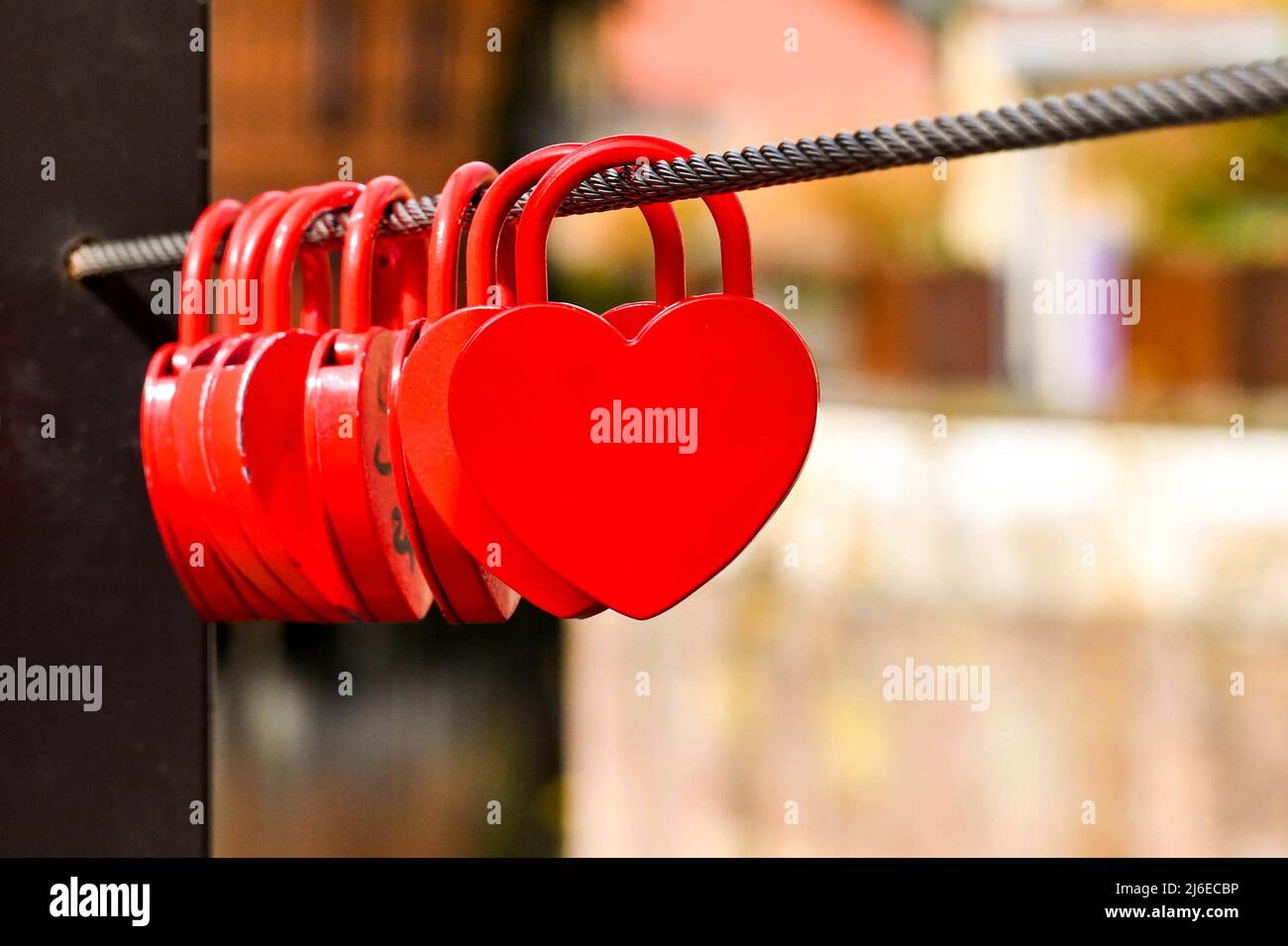 Fila di piccole serrature rosse a forma di cuore in metallo bloccate a un cavo in acciaio. Nessuna gente. Foto Stock
