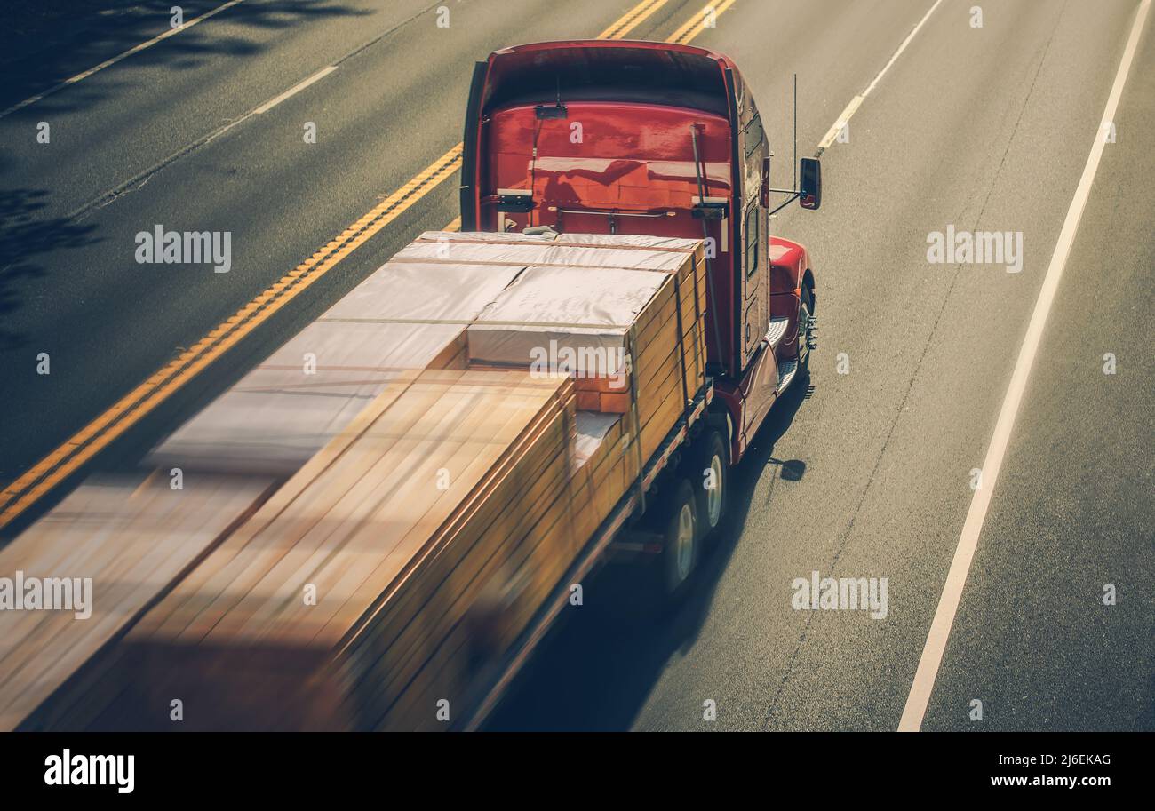 Semi-autocarro ad alta velocità con rimorchio caricato con travi e pianali in legno. Trasporto per impieghi gravosi. Foto Stock