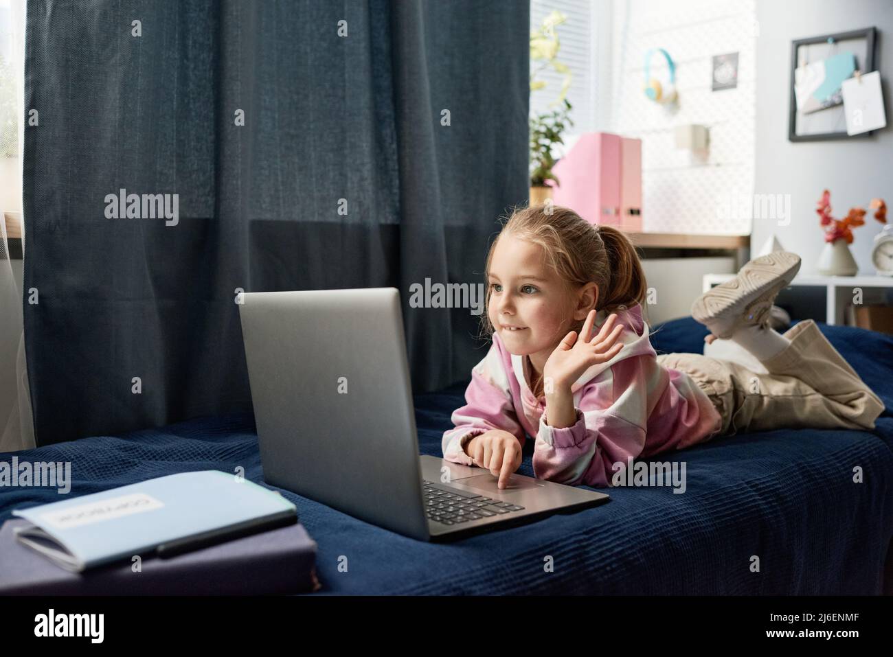 Simpatica ragazza bionda-pelo sdraiata sul letto e con la mano mentre si parla con il tutor online Foto Stock