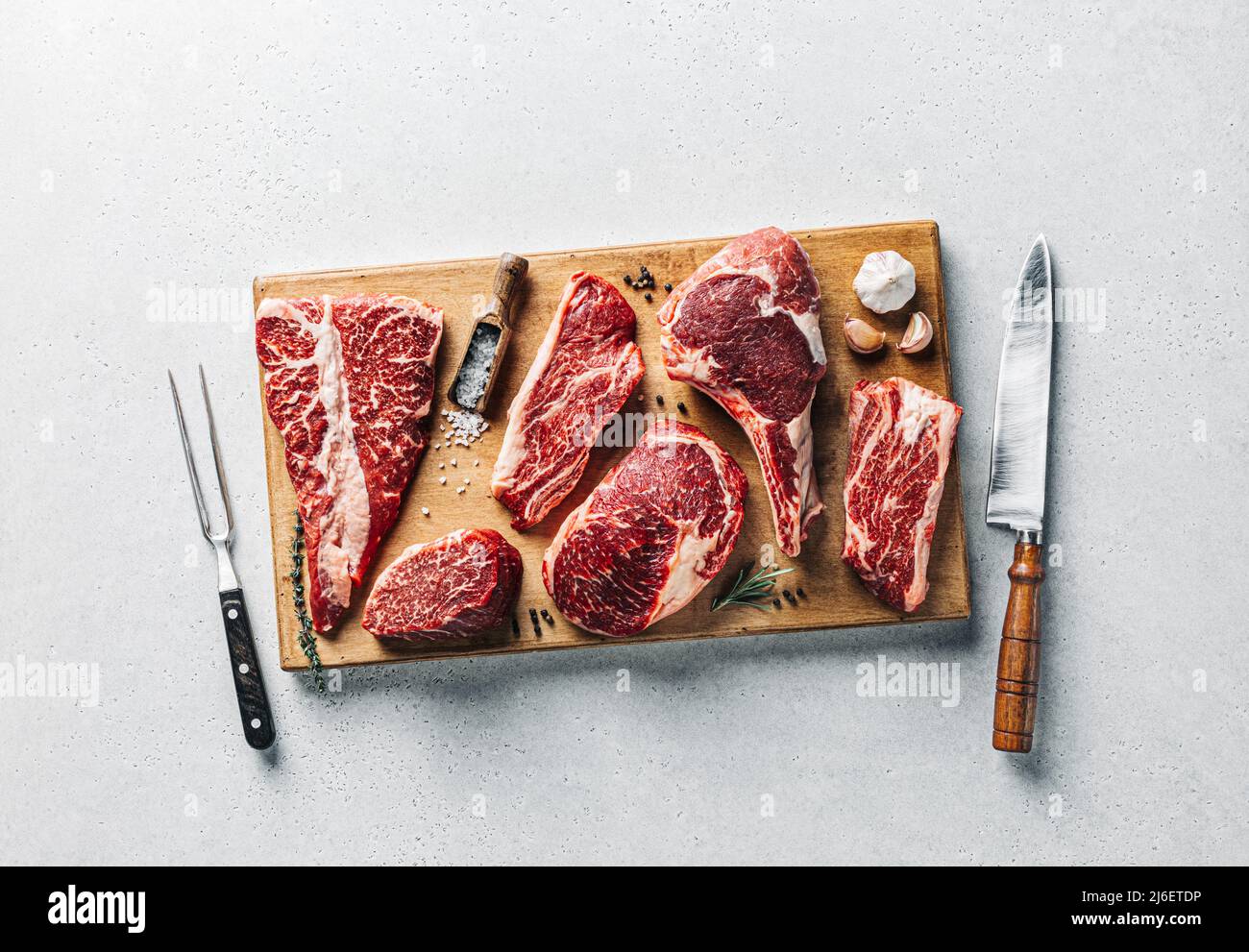 Bistecche di carne Angus prime su tavola di taglio in legno su fondo di cemento grigio Foto Stock