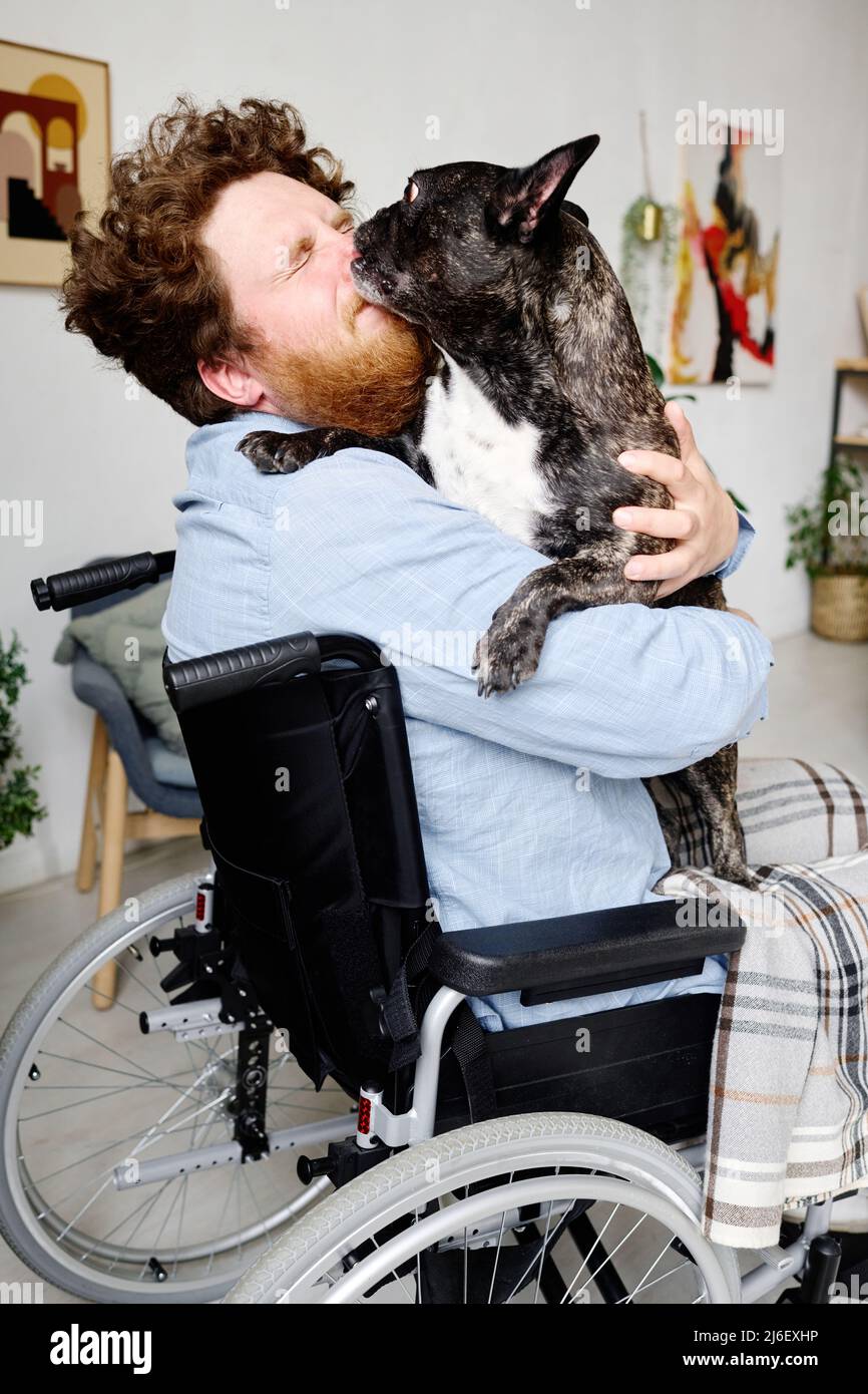 Giovane ragazzo guardato in sedia a rotelle chiudendo gli occhi mentre il suo animale lo baciava in faccia Foto Stock
