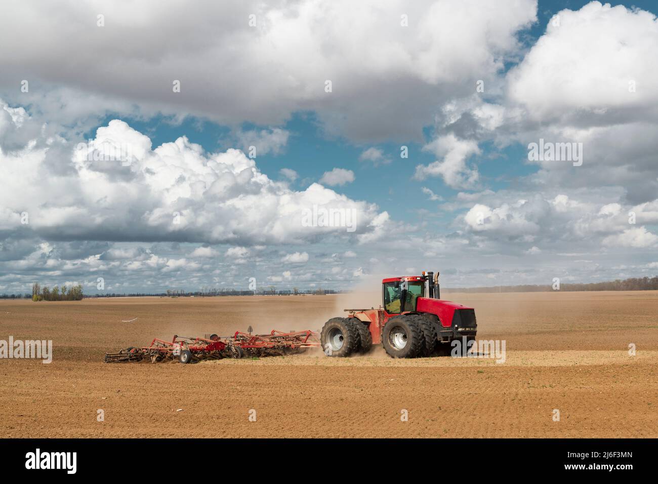 Trattore rosso sul campo arato. Lavori agricoli di primavera in Ucraina. Terreno coltivato e cielo con nuvole. Paesaggio di campagna Foto Stock