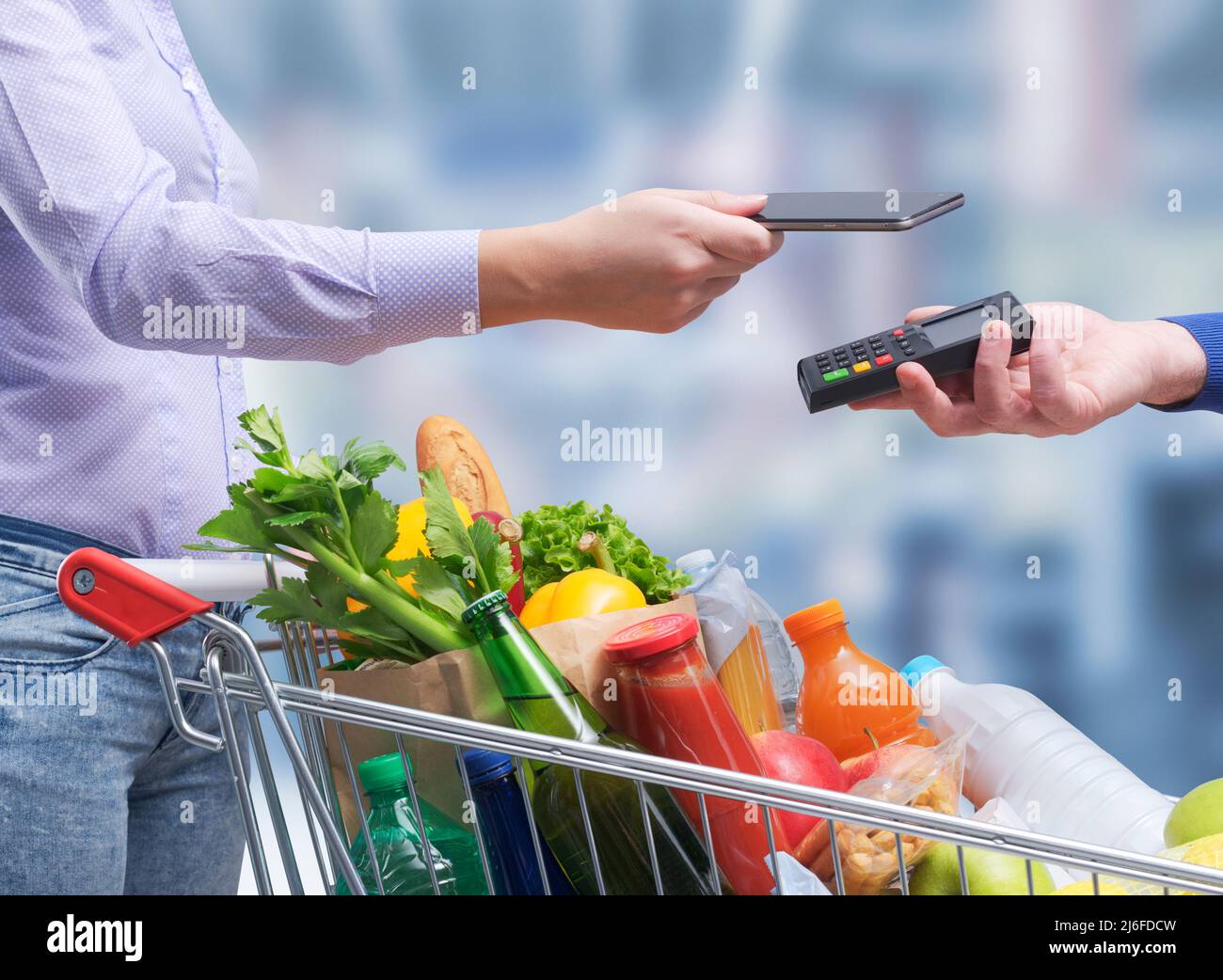 Donna che paga per generi alimentari utilizzando il suo smartphone, NFC Payments Concept Foto Stock