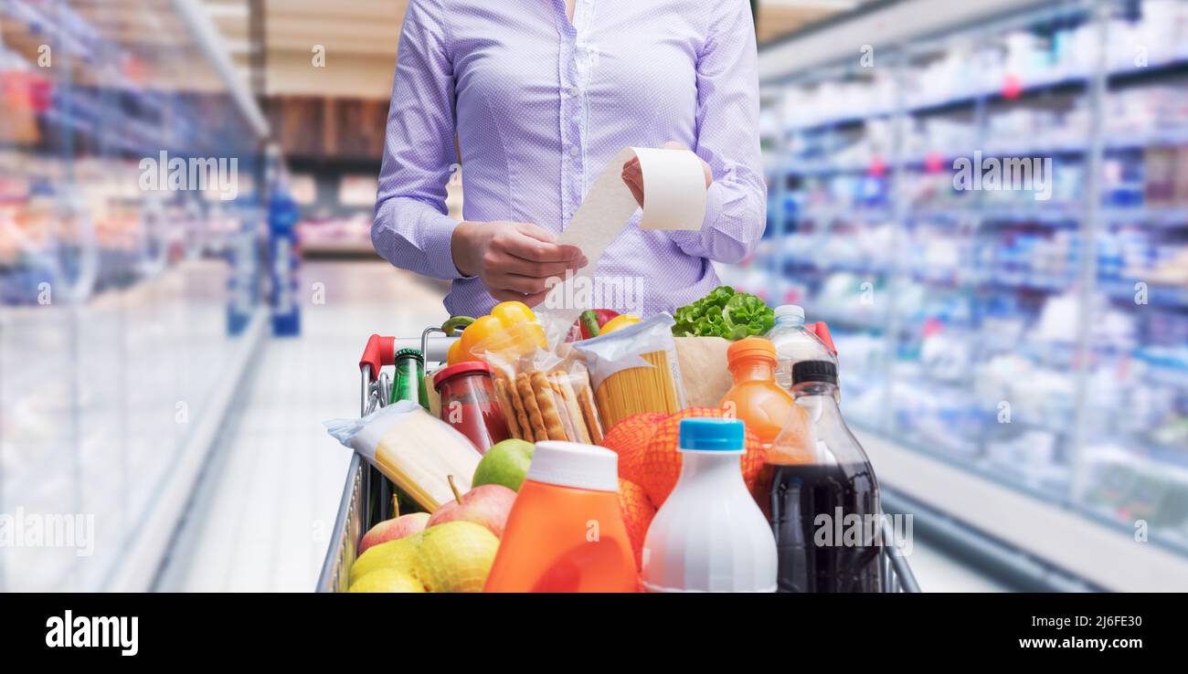 Donna che spinge un carrello e controllare una ricevuta della drogheria, negozio di alimentari e le spese concetto Foto Stock