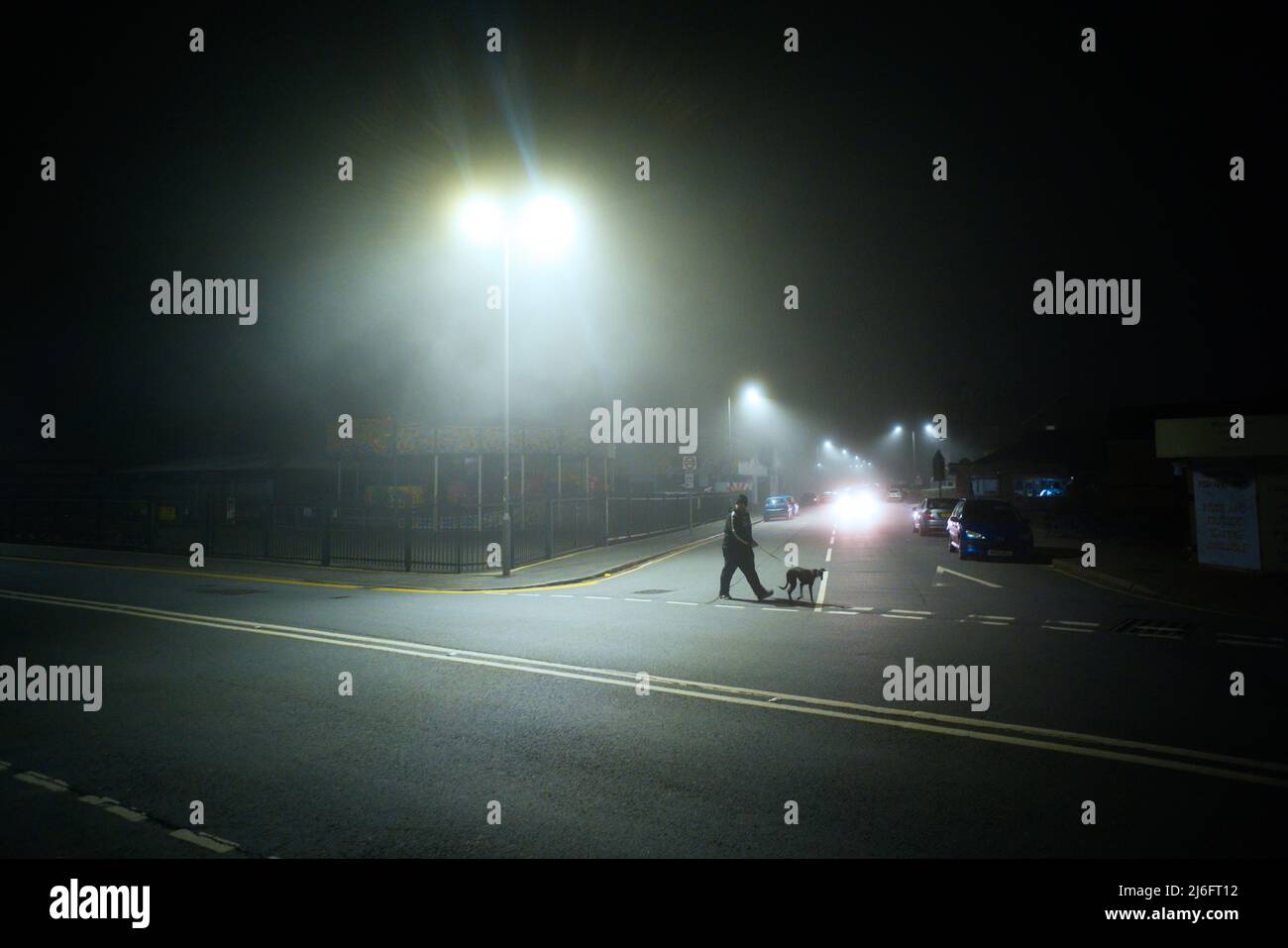 Sgranato d'atmosfera di strada di notte con l'uomo che prende un cane da levriero per una passeggiata Foto Stock