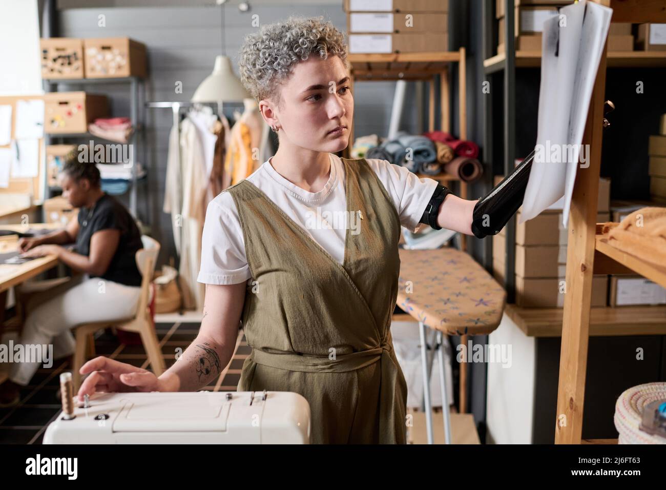 Giovane e serio marinaio con braccio parziale che guarda schizzo sulla carta mentre si scelgono nuovi modelli di abbigliamento per la collezione moda Foto Stock