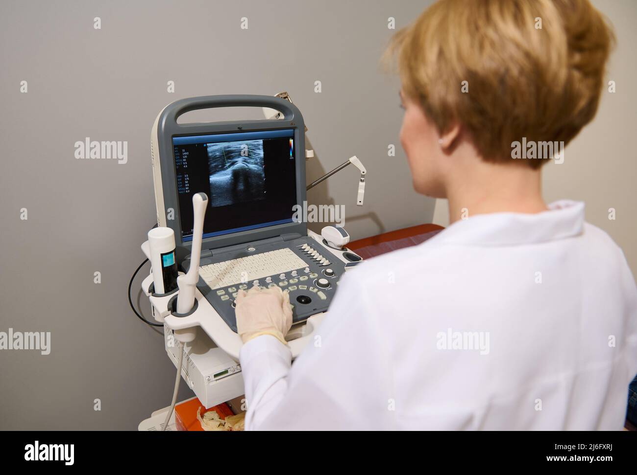 Soft focus sulla moderna macchina a ultrasuoni, Ultrasonografia USG. Vista posteriore di un medico radiologo caucasico durante l'esame a ultrasuoni Foto Stock