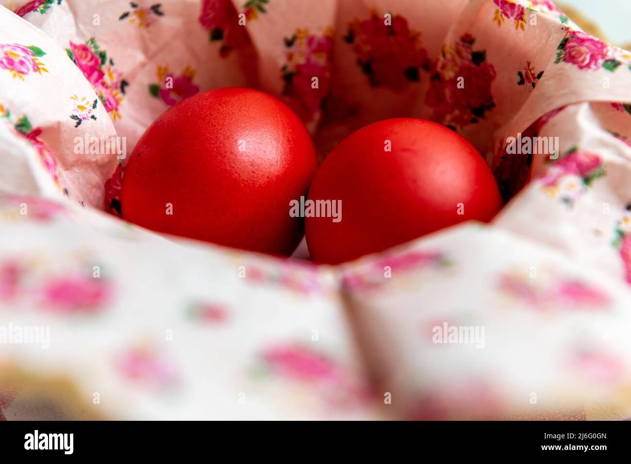 Due uova di Pasqua tinte rosse in una ciotola con tovaglioli di carta floreale. Foto Stock