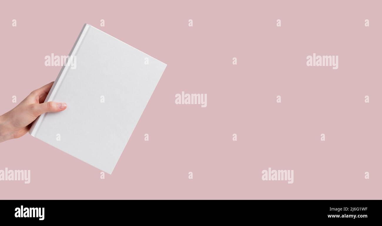 Banner con mano che tiene il mockup del libro su sfondo rosa e pastello. Istruzione, lettura, conduzione della ricerca, acquisizione di un concetto di conoscenza. Spazio di copia. Foto di alta qualità Foto Stock