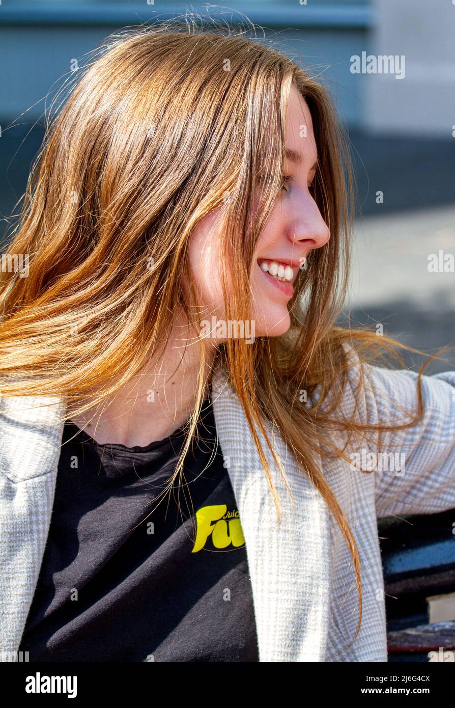 Una bella giovane donna seduta fuori godendo il caldo sole di aprile nel centro di Dundee, Scozia Foto Stock