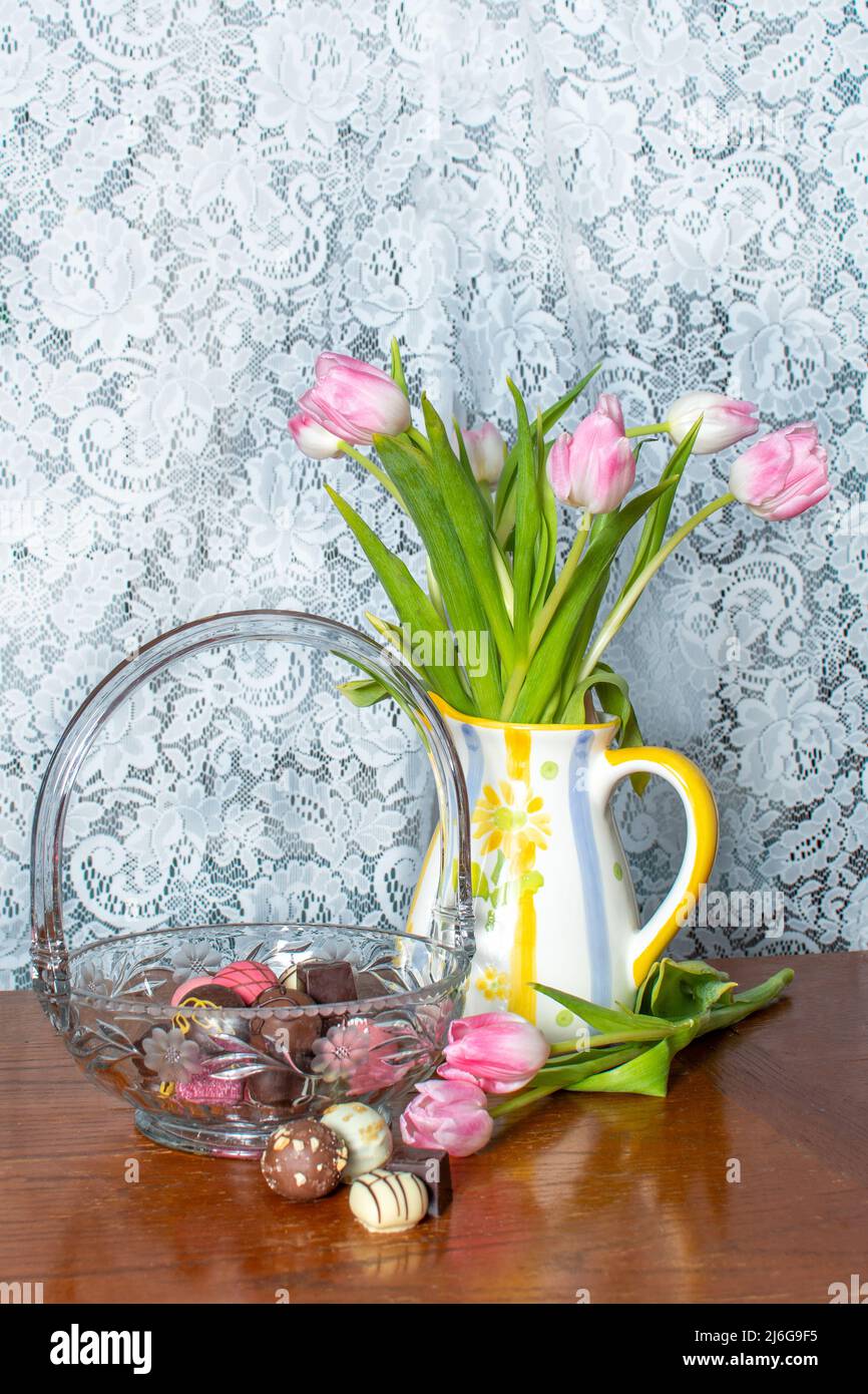 il piatto di caramelle in cristallo contiene cioccolatini gourmet, mentre una caraffa decorativa contiene tulipani rosa Foto Stock