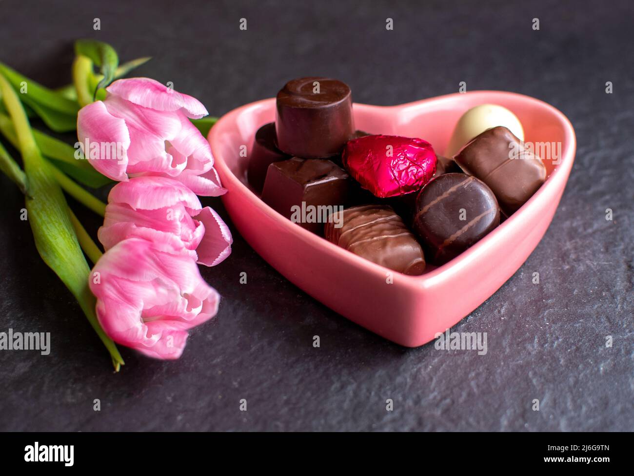 tulipani rosa e un piatto di caramelle a cuore rosa pieno di cioccolatini gourmet Foto Stock