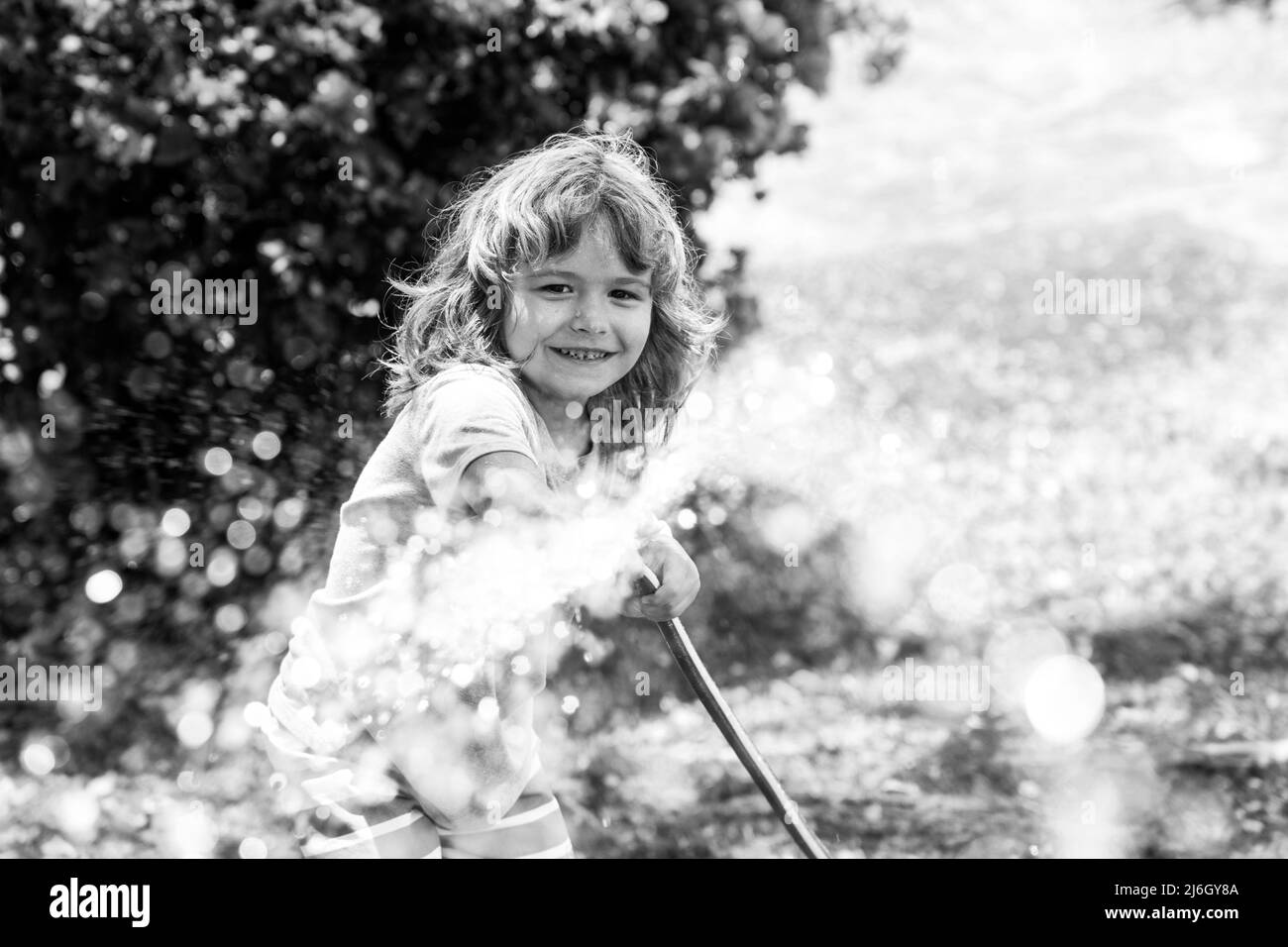 Bambini annaffiatura fiori e piante in giardino. Bambino con tubo dell'acqua nel cortile. Giardinaggio bambini. I bambini si divertono all'aperto a casa. Foto Stock