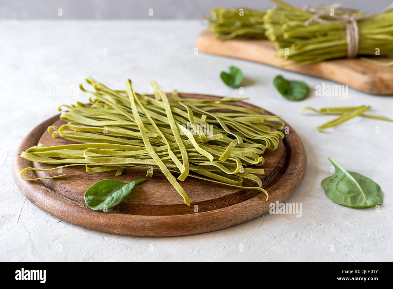 Fettuccine di pasta cruda con spinaci su tagliere in legno e fondo in calcestruzzo Foto Stock