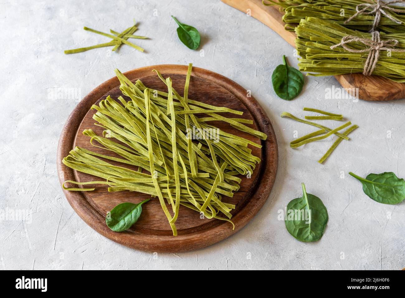 Fettuccine di pasta cruda con spinaci su tagliere in legno e fondo in calcestruzzo Foto Stock