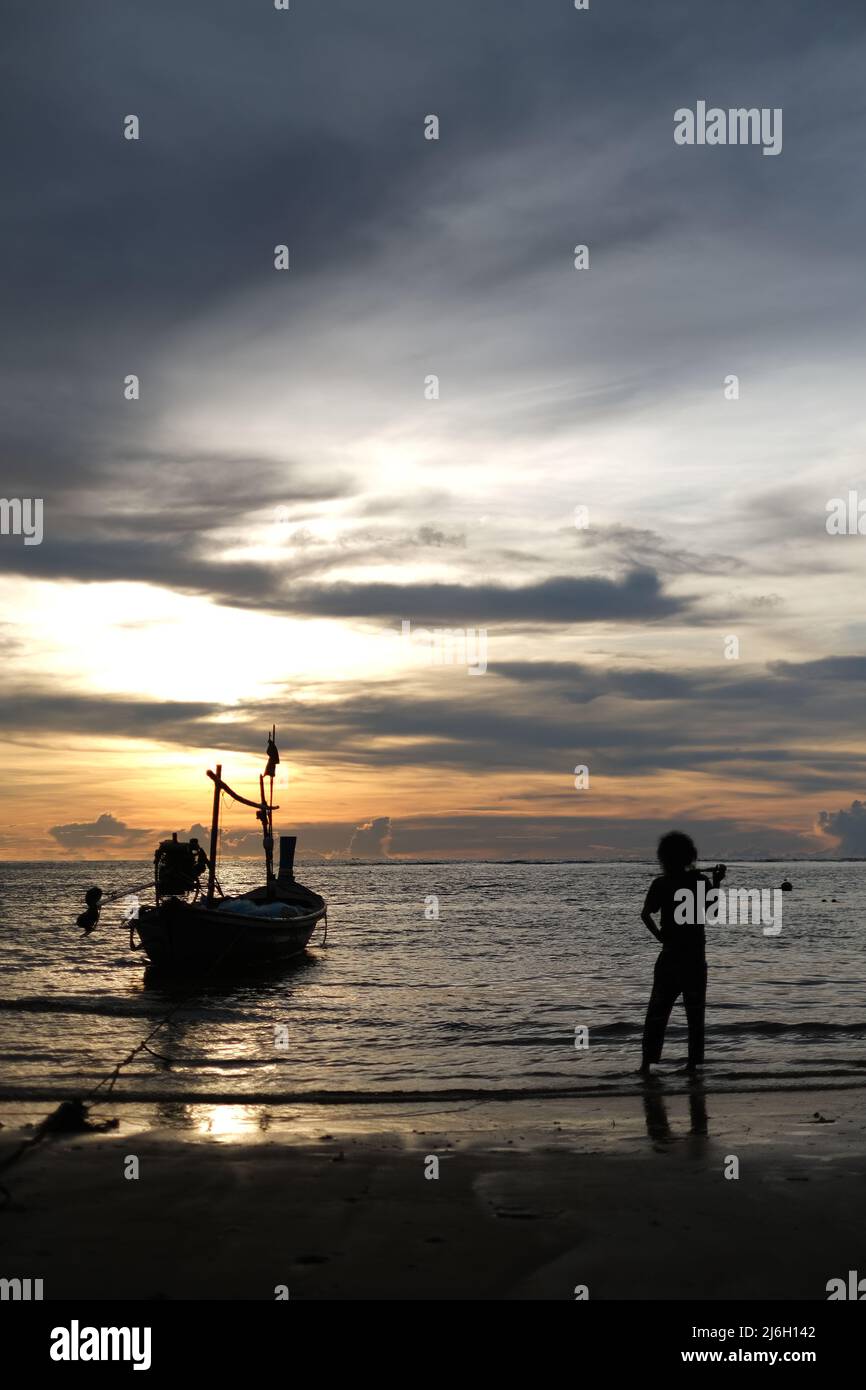 Una barca da pesca e un pescatore, illuminati dal sole, pronti a partire per un viaggio notturno al mare delle Andamane Foto Stock