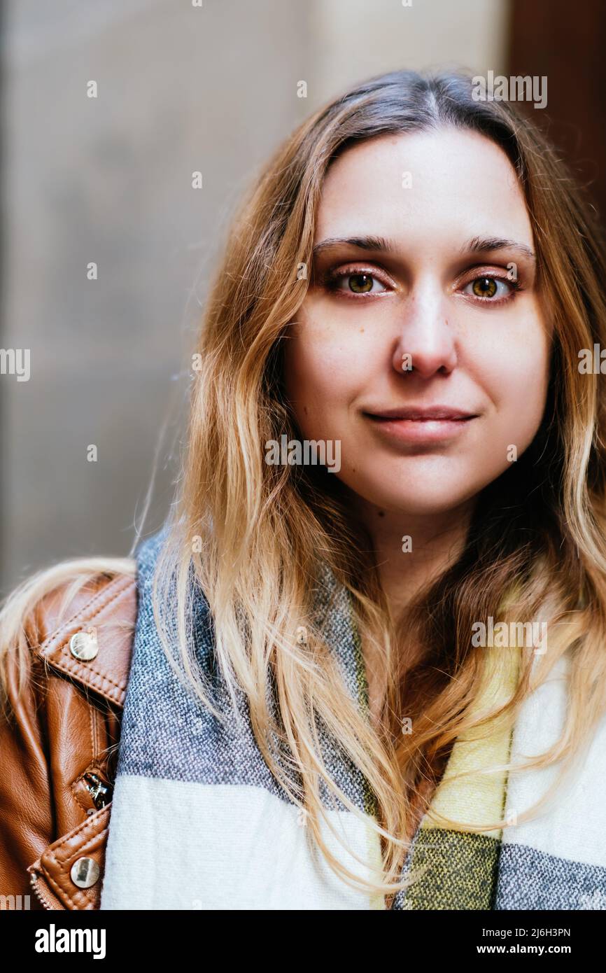 Attraente donna in outerwear con lunghi capelli marroni guardando la macchina fotografica mentre si trova sulla strada vicino all'edificio in città Foto Stock